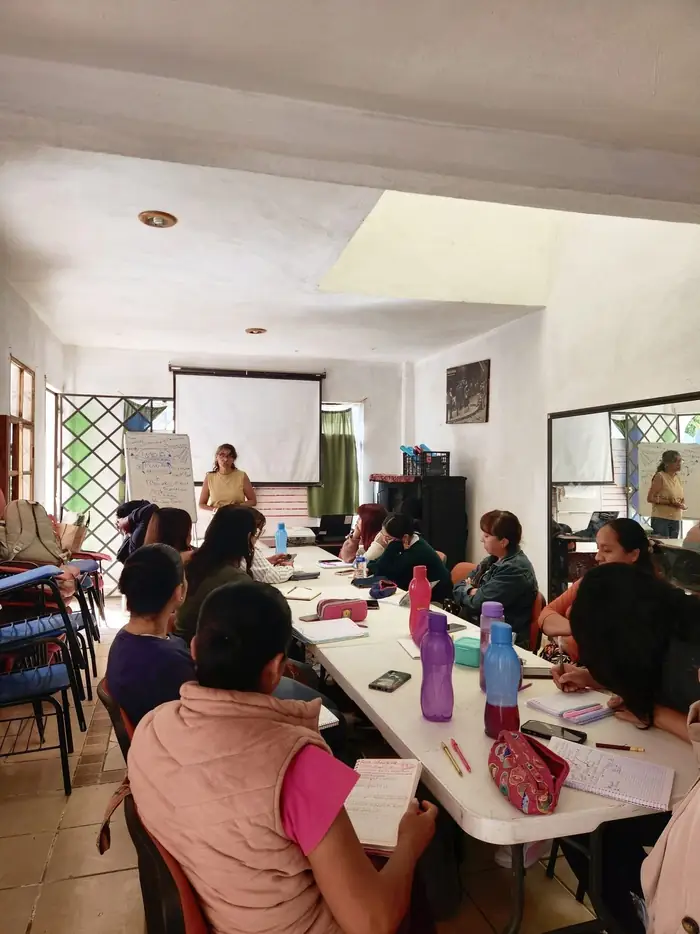 Reunión de formación docente alrededor de una mesa larga, con rotafolios y proyector
