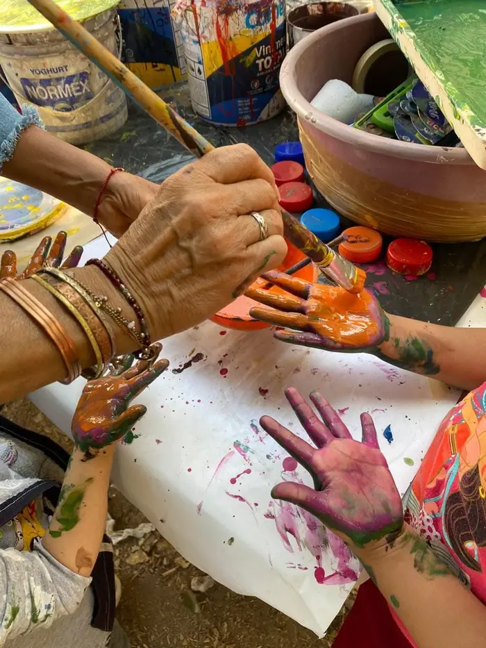 Manos de una maestra y de una niña cubiertas de pintura sobre un papel en el taller de arte