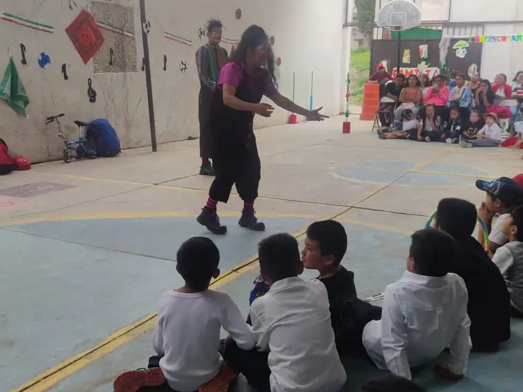 Función de teatro clown en el patio, con niños de preescolar y primaria sentados mirando